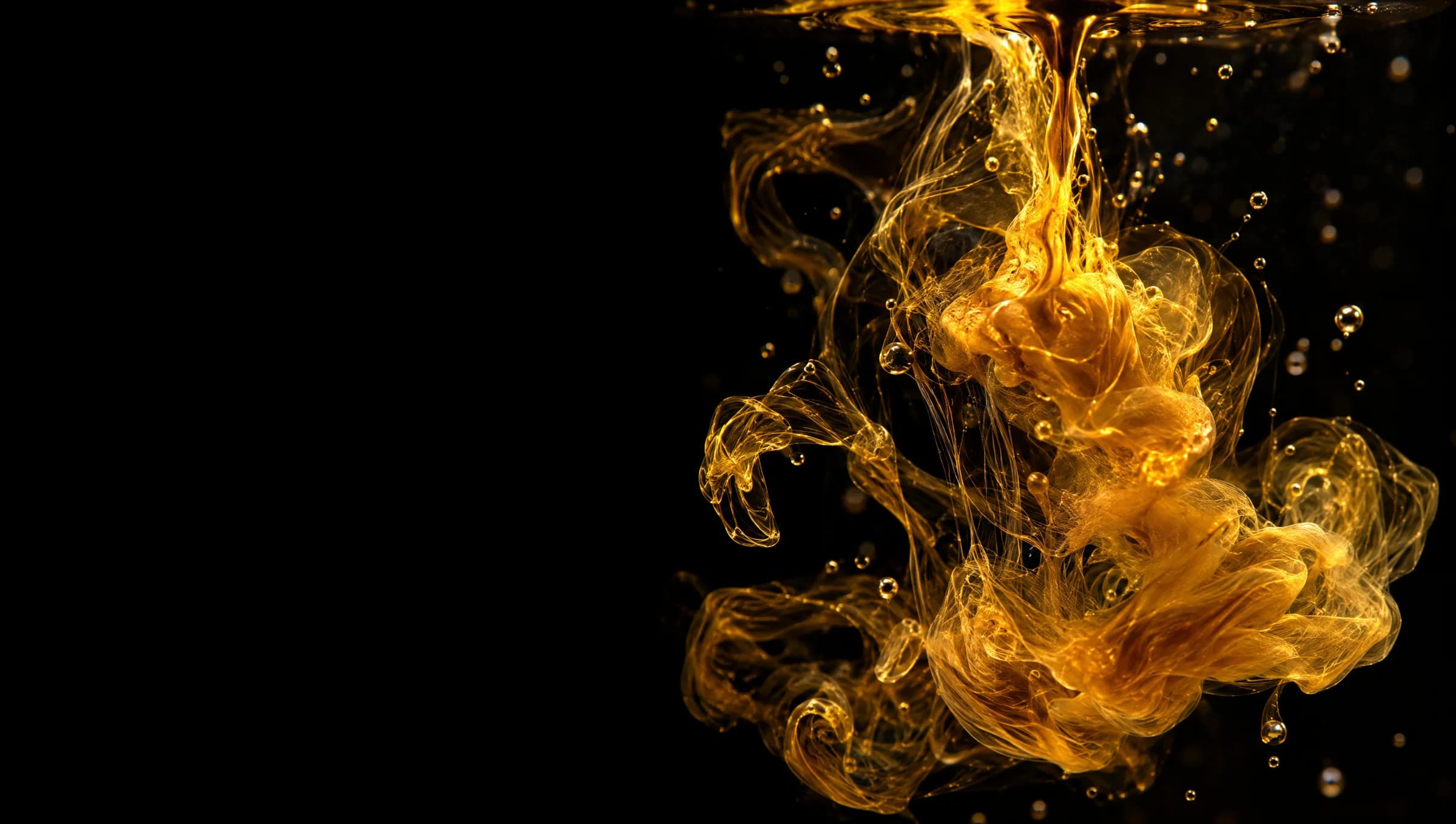 A drop of liquid gold dispersing into clear water in fine luminous threads.